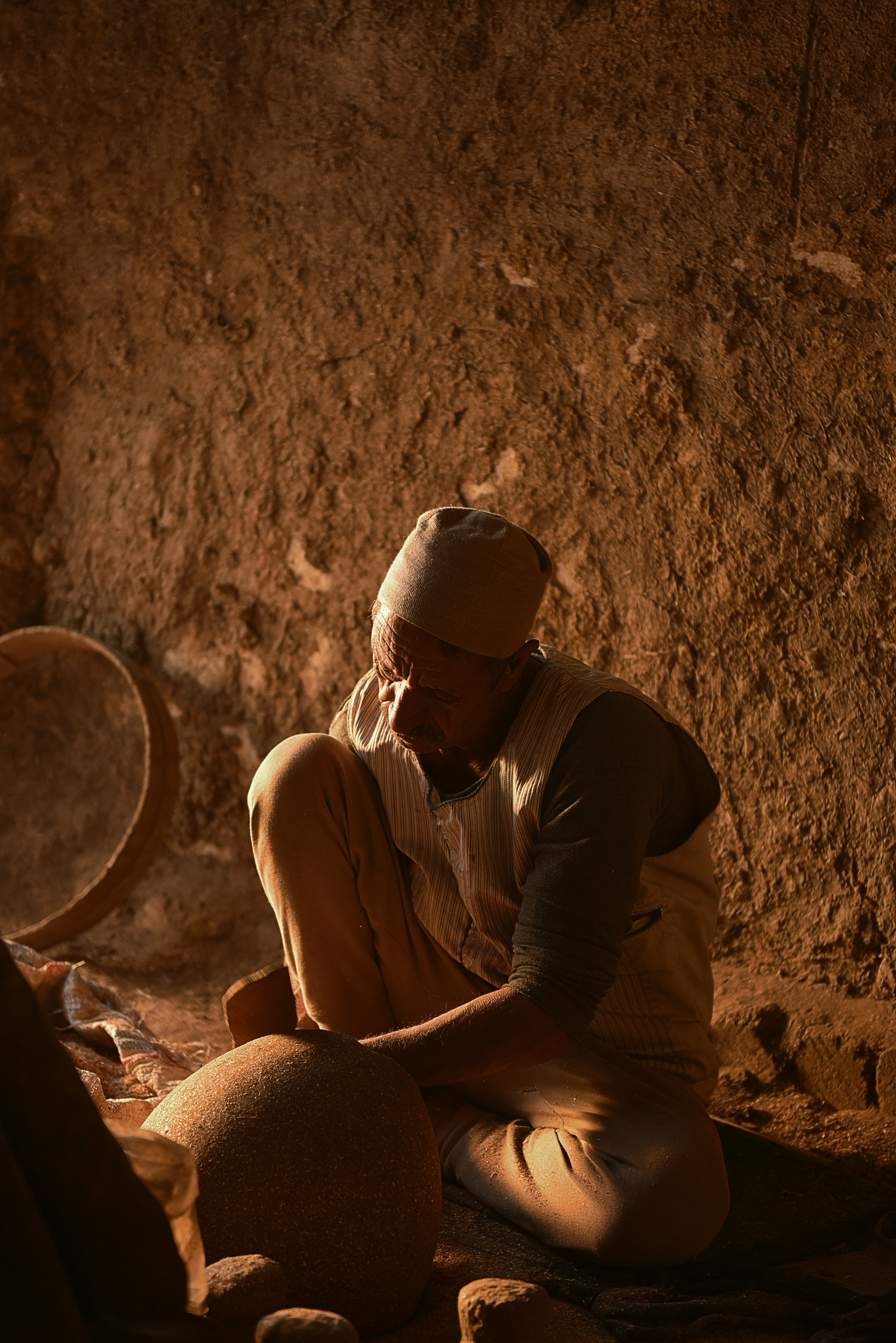 man in white tank top and brown hat sitting on brown sand during daytime